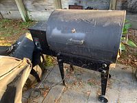 Photo of the closed black metal Traeger smoker with embossed logo and mountain design on the lid, standing on legs with two wheels