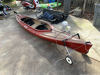 Full view of red and black speckled tandem kayak with two cockpits, deck bungee lines and attached two-wheeled cart
