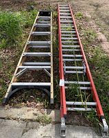 Two ladders laid side by side on grass and pavement.