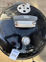 Top view of black Weber barbecue lid showing temperature gauge and vent with handle
