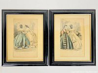 Two framed antique fashion prints shown side by side on a white background, black frames with gold inner trim, cream mats, prints slightly yellowed with age