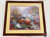 Photo of framed Luminism painting showing a cozy illuminated cottage surrounded by autumn foliage and a small waterfall with swans in the foreground.