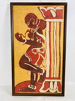 Full view of framed batik cloth showcasing stylized figure with bead jewelry and architectural pillar in red, white, and yellow.