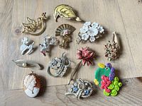 Full view of 11 assorted vintage brooches featuring floral, animal, and cameo designs on a wooden surface.