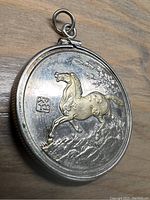 Front side of the coin mounted in the pendant frame featuring a raised horse image and Chinese character.