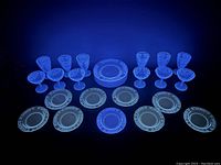 Set of blue acid etched dinner and luncheon plates, parfait and sherbet glasses glowing under black light revealing uranium content.
