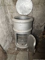 Front view of the cylindrical ice box with open lid and front door revealing interior wire racks.