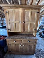 Front view of closed two-piece wooden cupboard with upper and lower cabinets, porcelain knobs, and metal hinges.