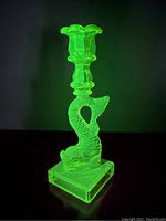 Uranium glass candleholder glowing bright green under UV light, showing full profile with fish design and triple candle cup.