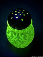 Sugar shaker glowing bright green under black light showing uranium glass fluorescence and white opalescent lace decoration.