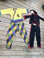 Yellow, purple, and green harlequin and theme-matching costumes laid flat on a wooden floor