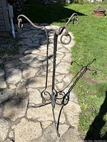 Full view of wrought iron Victorian fern stand outdoors on stone pavement showing overall shape and condition.