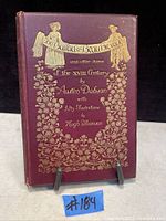 Front cover of antique book 'The Ballad of Beau Brocade and Other Poems' showing maroon cover with gold embossed decorative floral patterns and title banner held by two figures.