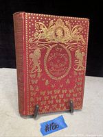 Front cover showing red hardcover with gold leaf embossed decorations, butterflies, cherubs, and title text.