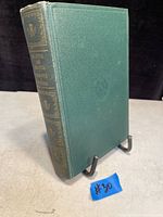 Photo of the green hardcover book standing on a stand, showing spine with the title and decorative gilt detailing.