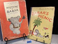 Photo of two antique 1939 children's books: 'Histoire de Babar' in French and 'Babar's Picnic' in English, both standing upright with visible age and wear on covers.