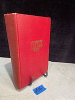 Front cover of the antique hardcover book, showing red cloth binding with gold embossed bell design and faded spine.