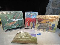 Front view of the 4 vintage kids books Parsley, Madeline in London, The Tortoise & The Hare, and Miss Rumphius on display stands and surface.