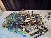 Overview of a large pile of assorted wristwatches featuring various bands and dial styles representing multiple well-known brands.