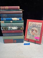 Image showing the full lot of 12 vintage books stacked and the book 'Blasts from a Pan's Horn' on display stand.
