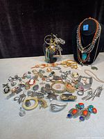 Full overview of all jewelry items including necklaces on display bust, bracelets on stand and scattered pins, brooches, rings and earrings.