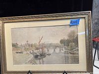Framed watercolor painting showing a riverside scene with boats, bridge, and buildings.