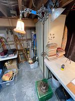 Full view of antique bridge floor lamp showing cast iron base, adjustable arm with two lamp sockets and glass shades, standing in a basement-style room.