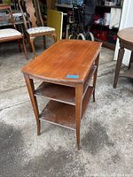 Front and side view of antique mahogany end table showing top surface, two shelves, and curved legs on concrete ground.