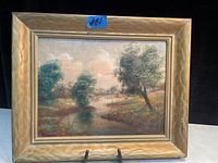 Framed antique oil on board painting showing a landscape with trees and a reflective body of water