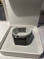 Apple Watch with stainless steel case and Milanese loop band displayed in original Apple Watch box, watch screen off.