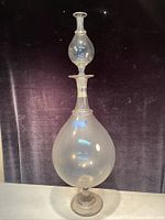 Full view of tall clear glass Victorian apothecary bottle with stopper, showing general shape and condition.