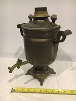 Photo showing front angle of vintage handmade brass and copper samovar with wooden handles and brass base next to tape measure for scale.