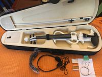 Open case displaying white electric violin, bow, earphones, cables, and extra strings set