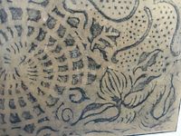 Close-up image showing details of black pastel patterns including swirling lines and floral motifs on brown paper.