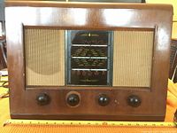 Front view showing wooden cabinet with fabric speaker grills and four wooden control knobs on the front.