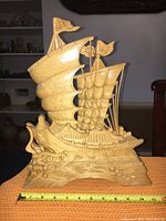 Front and side view of the hand-carved wooden ship sculpture on a table with measuring tape in front showing size approximately 14.5 inches tall.
