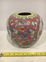 Photo shows the overall front view of the vintage Chinese ceramic jar, with floral and bird hand-painted designs on a pink and white background. A yellow measuring tape placed in front indicates width around 9 inches.