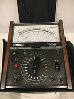 Close-up of the Sanwa N-301 electrical tester front panel showing the analog meter, rotary dial with measurement units, input terminals, toggle switch, and indicator labels.