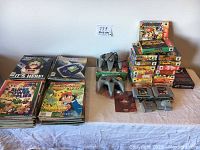 Wide view of two controllers, stacked N64 game boxes, loose cartridges and magazines laid out on table.