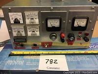 Full front view of the large metal tester with all meters and controls visible, including a ruler for scale.