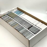 Box filled with baseball cards stored in sleeves and divided into three sections by cardboard supports, showing multiple rows of cards with different colors and thicknesses.