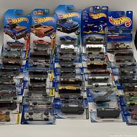 Display of multiple Hot Wheels toy cars in original packaging laid out in rows showing front of packages and variety of models.