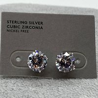 Pair of round cubic zirconia stud earrings on grey card marked 'Sterling Silver Cubic Zirconia Nickel Free'