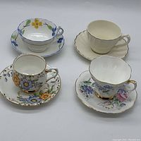 Four assorted teacups with matching saucers arranged in two rows on white background. Varied floral designs and colors. Includes both close and wider angled views.