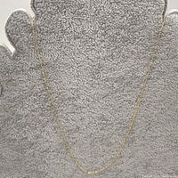 Full view of necklace laid flat on grey surface showing chain shape and length