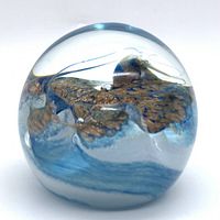 Front angle of paperweight showing blue and gold decorative inclusions inside clear crystal glass.