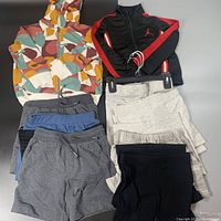Full lot showing colorful camouflage hooded jacket, Jordan track jacket, multiple pairs of shorts, and leggings