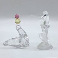 Both Swarovski crystal figurines shown: seal balancing pink and yellow balls, and seahorse on frosted base.