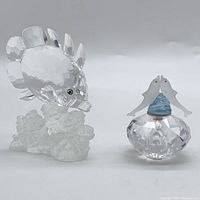 Front view showing both figurines: the butterfly fish on the left on coral base and the dolphin pair on the right on a faceted crystal base with blue swirl.
