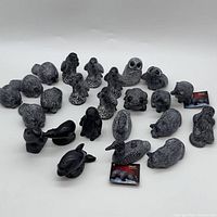 Group photo of all 24 soapstone animal sculptures arranged on a white background showing various animal figures including beavers, eagles, black bears, otter, owls, frog, loonies, orca, seals, and penguin.